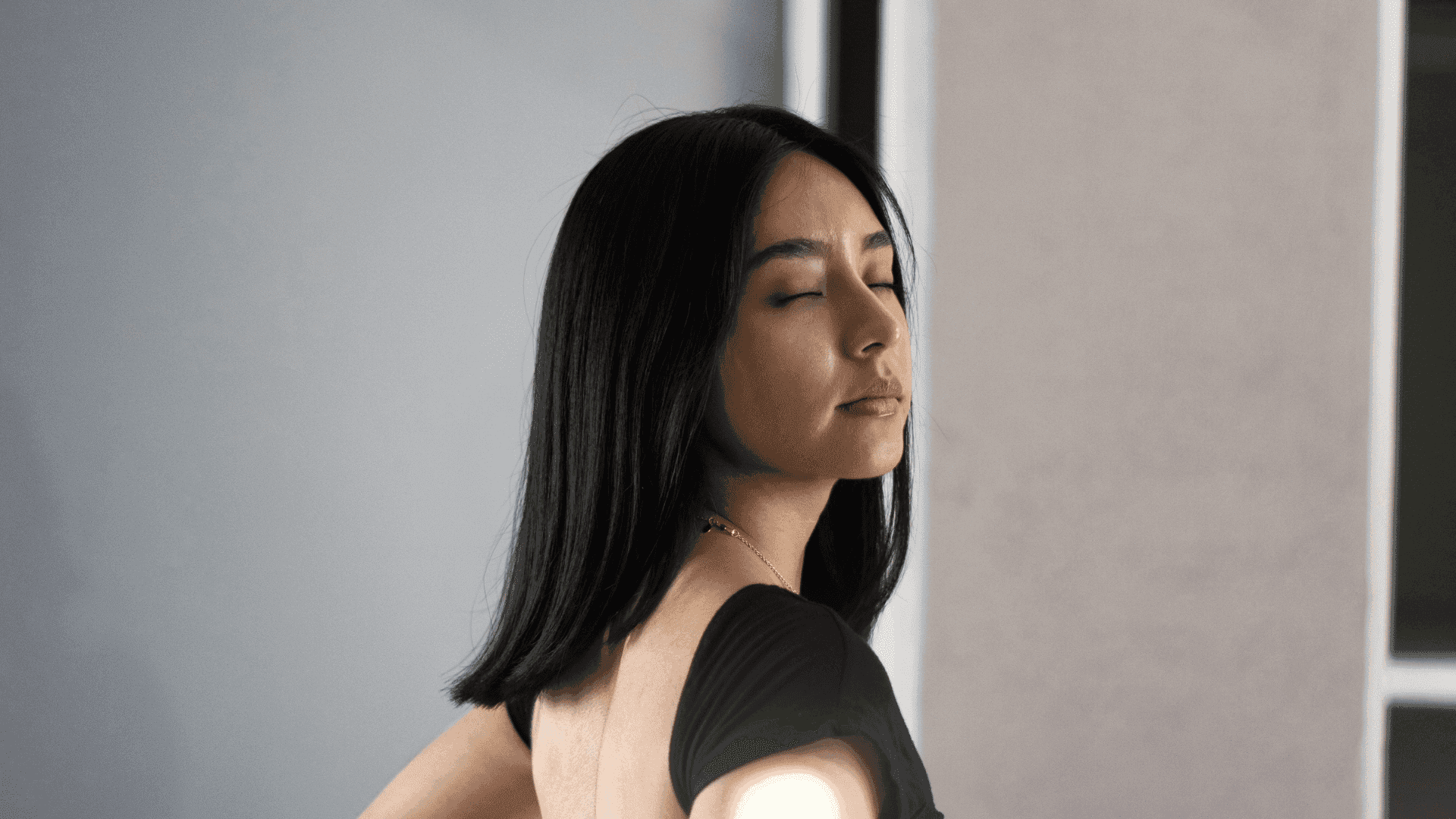 Woman with closed eyes and long hair, standing against a neutral background.