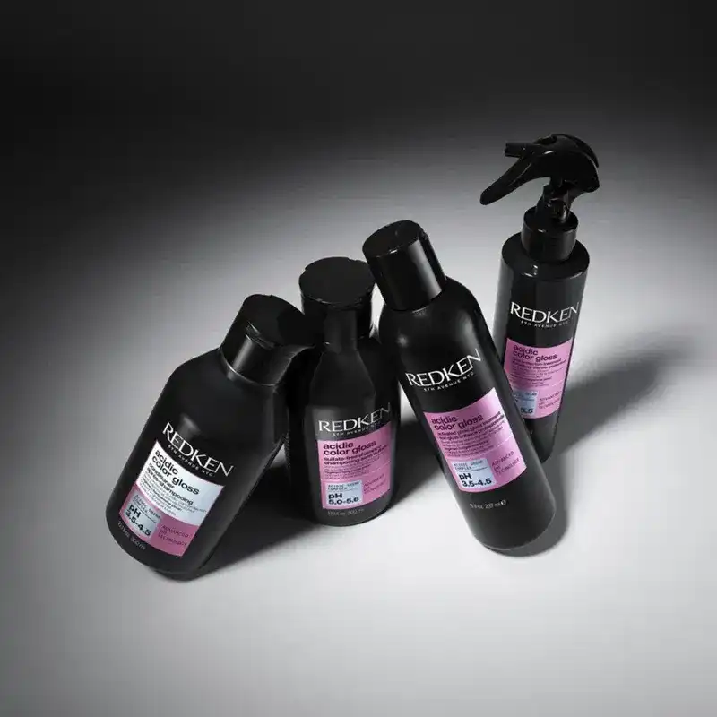 Four Redken hair care bottles with black design and pink labels on a dark background.