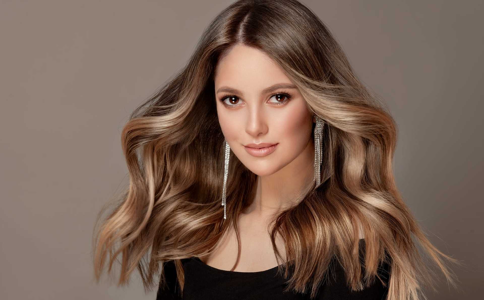 Woman with long, wavy brown hair and silver earrings, wearing a black top.