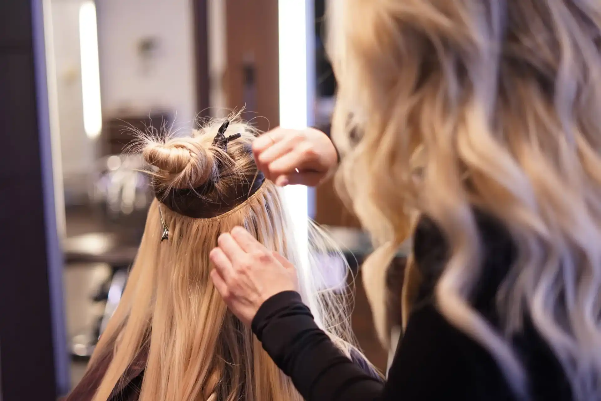 Hairdresser attaching blonde hair extensions in a salon setting.